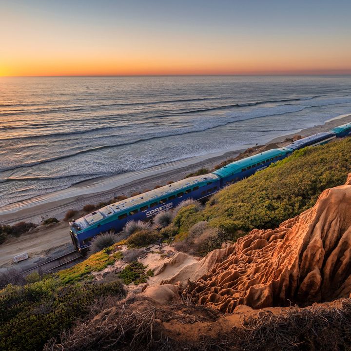 The Pacific Surfliner Amtrak train on a track in Del Mar, California that hugs the coastline and beach at sunset.