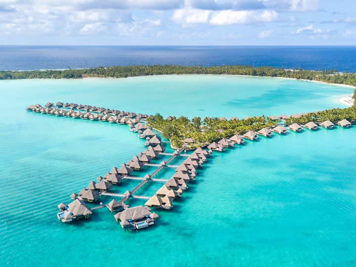 Rows of overwater villas atop bright blue water at The St. Regis, Bora Bora.