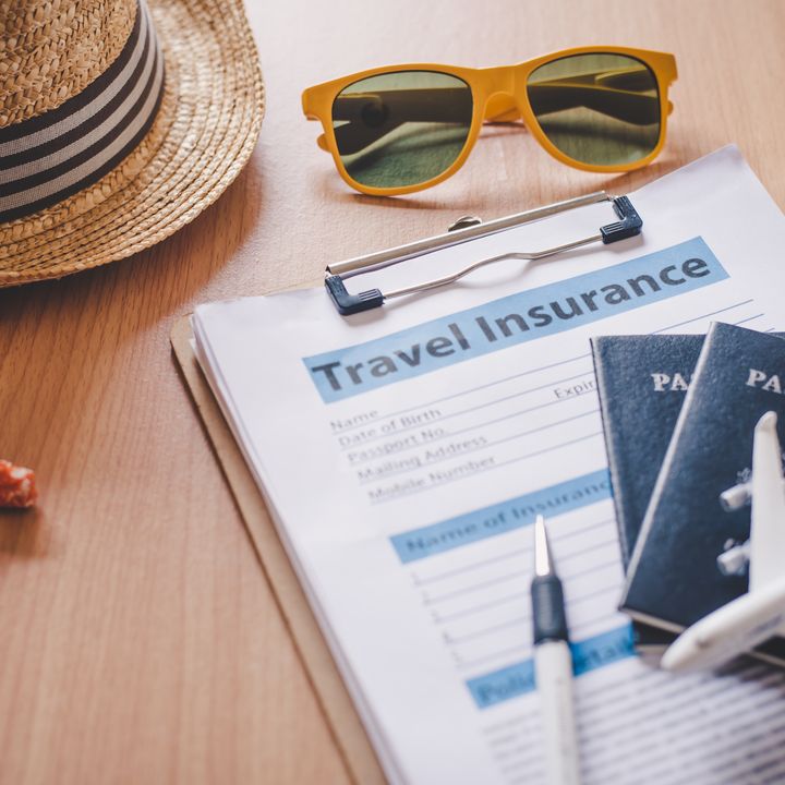 A clipboard with travel insurance paperwork plus passports, a pen, sunglasses, a hat, starfish, and toy plane and car.