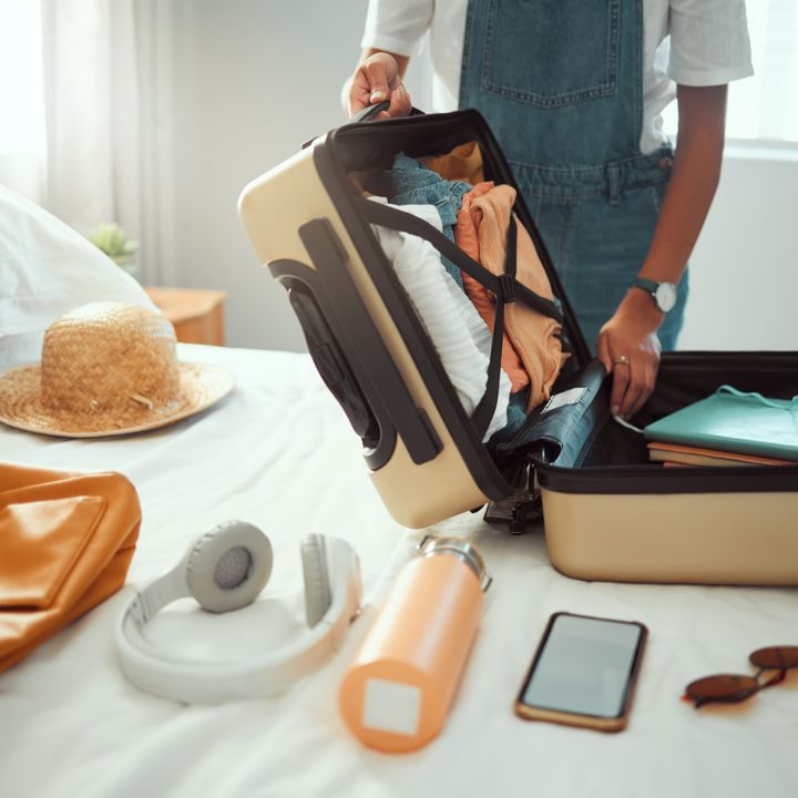 Different travel supplies laid out on a bed with a person packing an open suitcase.