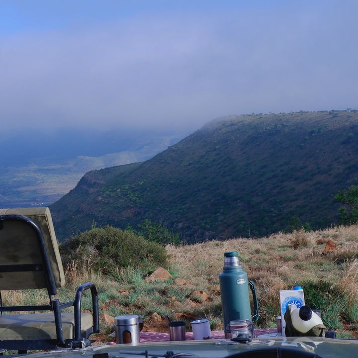 A picnic with a chair and a thermos and cups set up on blanket on a mountain.