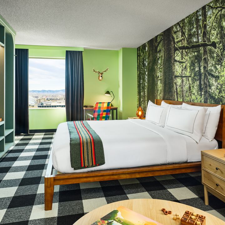 A camping themed room at The Curtis Hotel with woodsy wallpaper, a fireplace-style lamp, taxidermy, and other accents.
