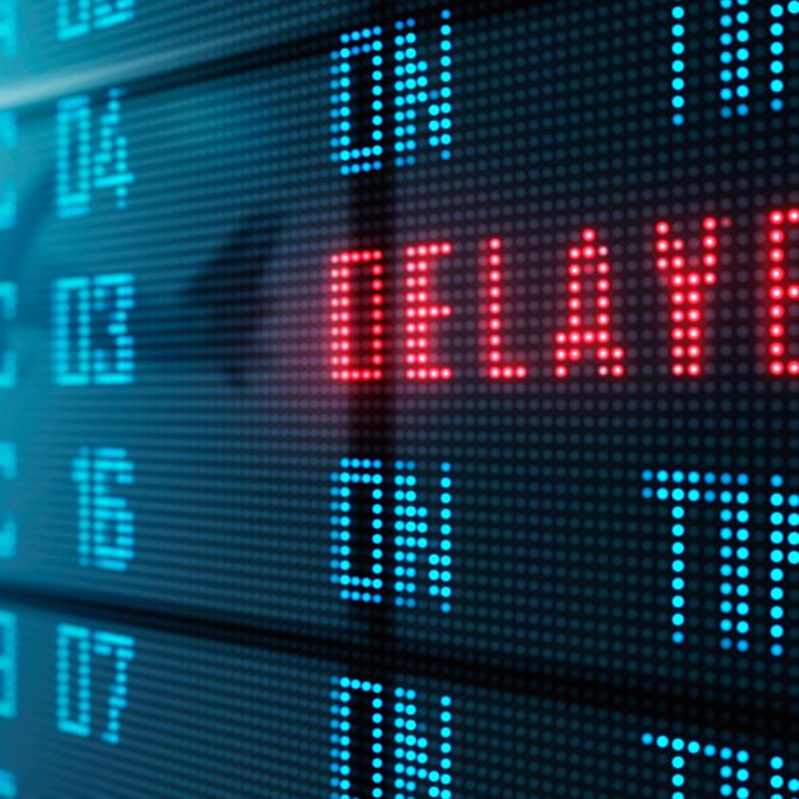 A flight status board in an airport says ‘delayed’ in red.