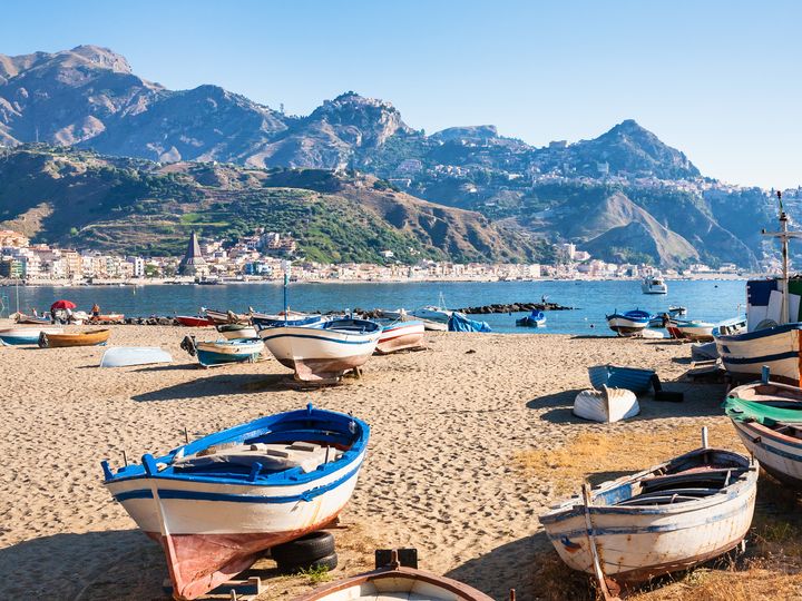 Several boats sit on the sand in Naxos with the sea and mountains behind them.