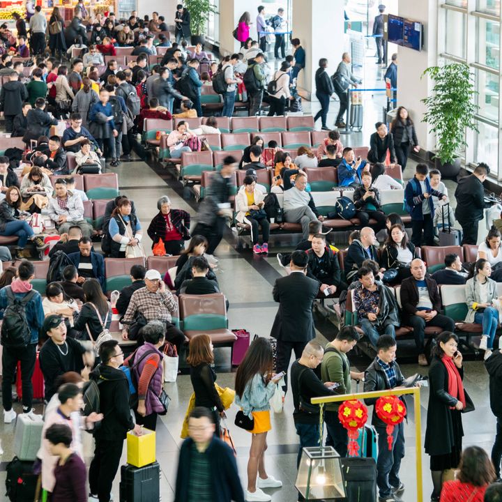 Large crowds of people wait in an airport, as seen from above.