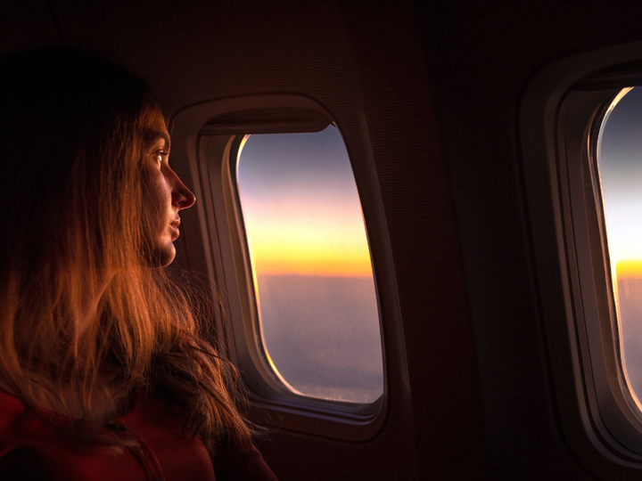 A woman sits at a plane window watching the sunrise.