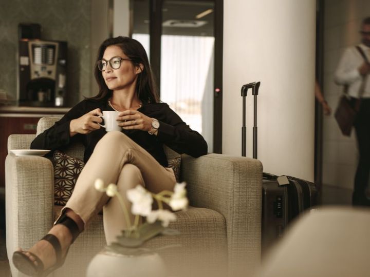 A woman sits in an airport lounge while holding a cup of coffee.