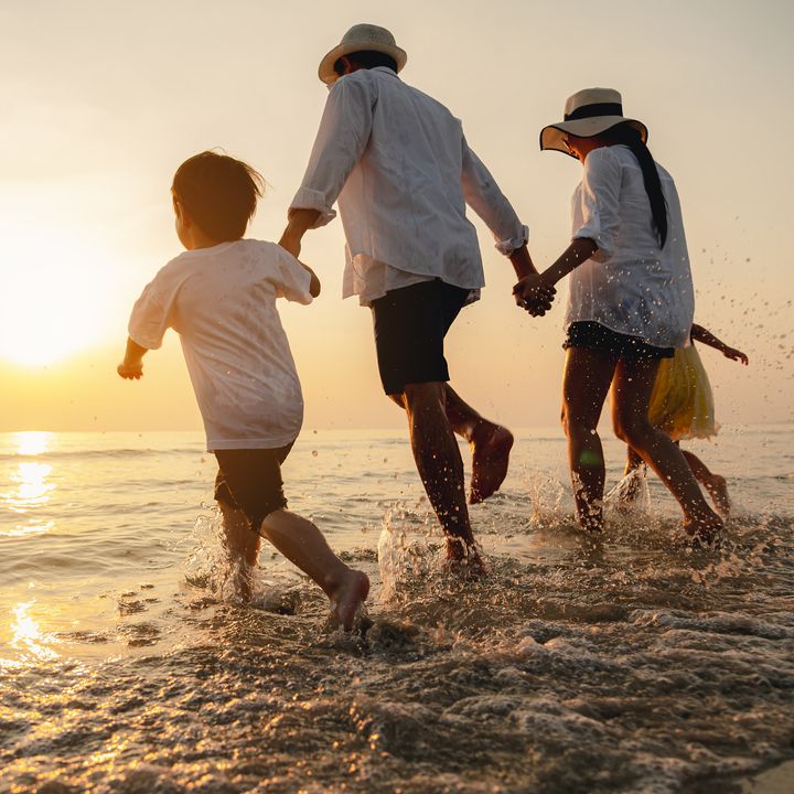A family holding hands and running toward the beach at sunset.