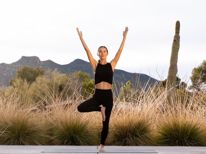 A woman is seen doing yoga in tree pose in a desert setting at Civana resort.