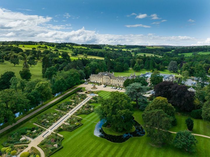 An English countryside estate-turned-hotel as seen from above surrounded by green lawns, bushes, and lush landscaping.