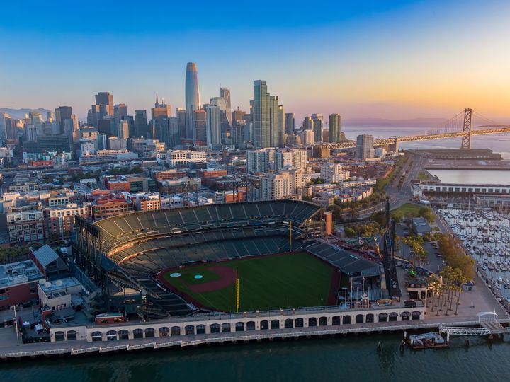 An aerial view over Oracle Park, home of the San Francisco Giants, in San Francisco with views of the city skyline behind it.