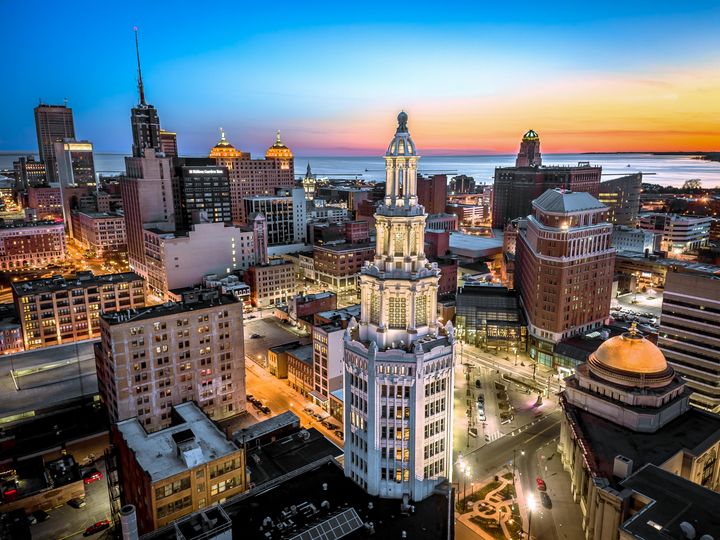 A skyline view of downtown Buffalo, New York, at sunset with pink and orange skies in the background and the Electric Tower skyscraper in the foreground.