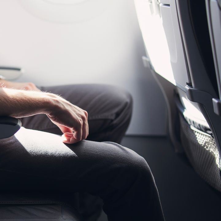 A man’s lower half is seen sitting on an airplane with lots of extra legroom.