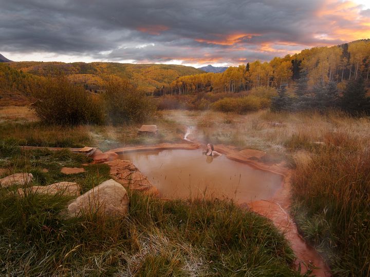 Steaming natural hot springs outside the bathhouse at Dunton Hot Spring, with dusk gray skies and forest in the background.