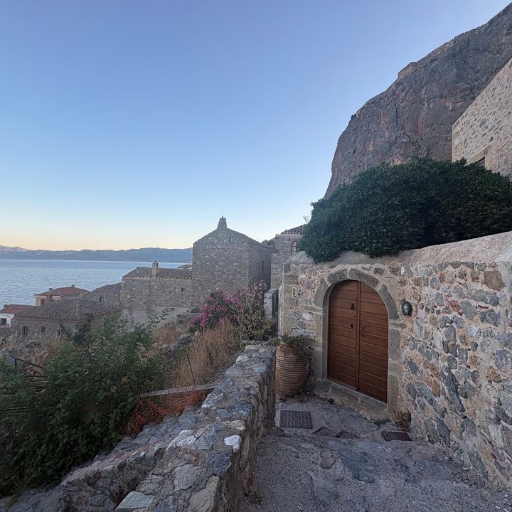 Stone walls and ocean views in Lower Town in Monemvasia with green bushes and pink flowers.
