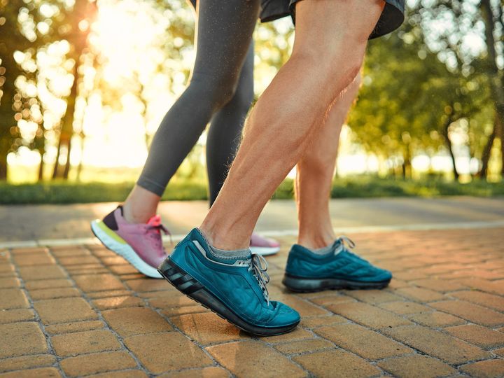 Close up of male and female legs in blue and pink sneakers on a cobblestone path in a park.