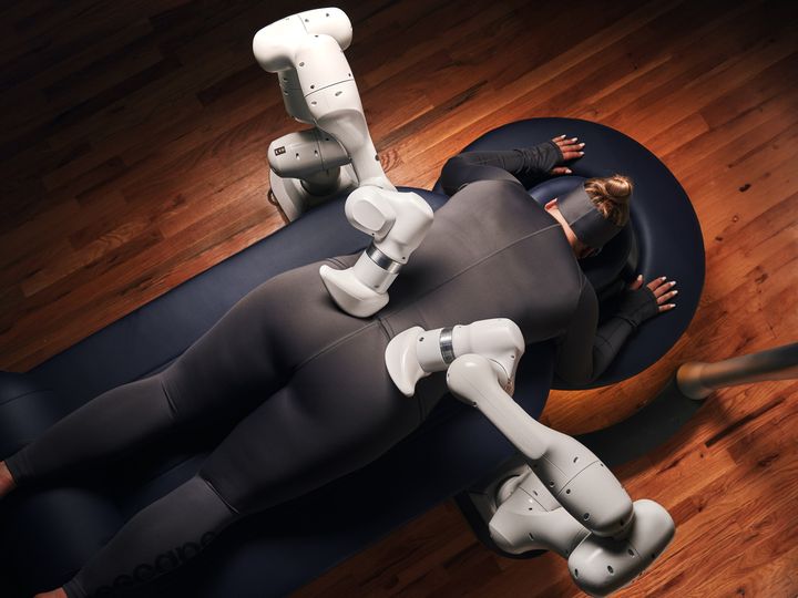 A woman is face down on a massage bed receiving a massage from the Aescape machine.