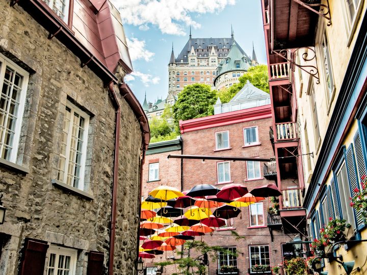 A view of Petit Champlain Street in Quebec City, Canada, with historic stone buildings on each side, decorative umbrellas, and a peek through at The Fairmont Chateau Frontenac.