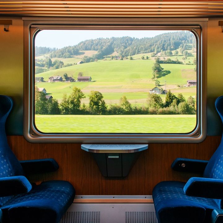 An interior view of a train car with two blue chairs facing each other and a rural scene out of the window.