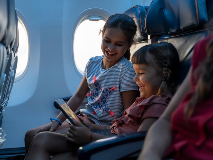 Two little girls travel by plane and look at an ipad next to the window.