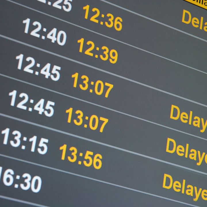 A flight status board is filled with delays showing the original times and the delayed times plus the word "delayed."