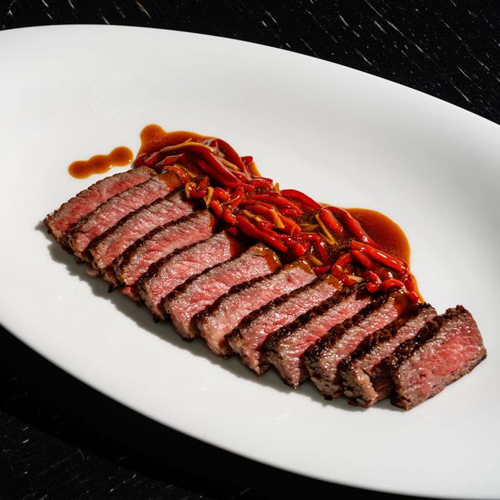 Neatly sliced pieces of medium rare steak arranged on a white plate next to red peppers in a brown sauce.