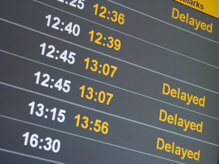 A flight status board is filled with delays showing the original times and the delayed times plus the word "delayed."