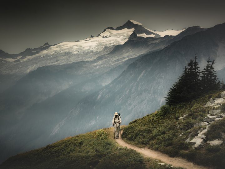 A male hiker is hiking through a valley pass on the back of snowy mountains in North Cascades National Park, Washington.