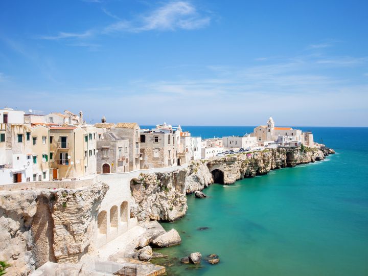 The town of Vieste in the Puglia region of Italy with a rock barrier extending into the sea topped with white buildings.