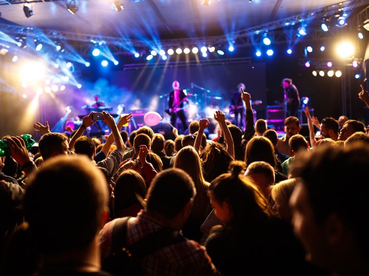 An eye-level view of a stage with a bunch of people with hands in the air at a concert.