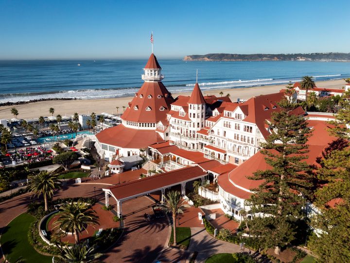 An aerial view of the red roofed Hotel del Coronado showcasing its beachfront location and entrance.