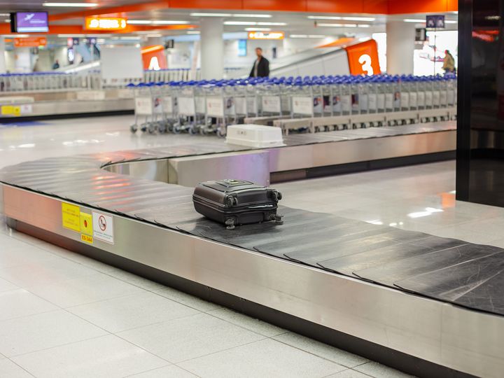 An empty luggage conveyor belt is seen with just one suitcase on it surrounded by airport luggage carts.
