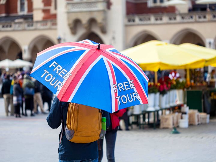 A tour guide holding a UK flag-themed umbrella that says free tour is seen in a European-looking square.