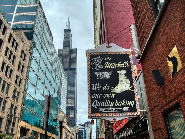 A sign on the side of a brick building on an urban street that says, “This is Lou Mitchell’s Restaurant and Bakery. We do our own quality baking.” 
