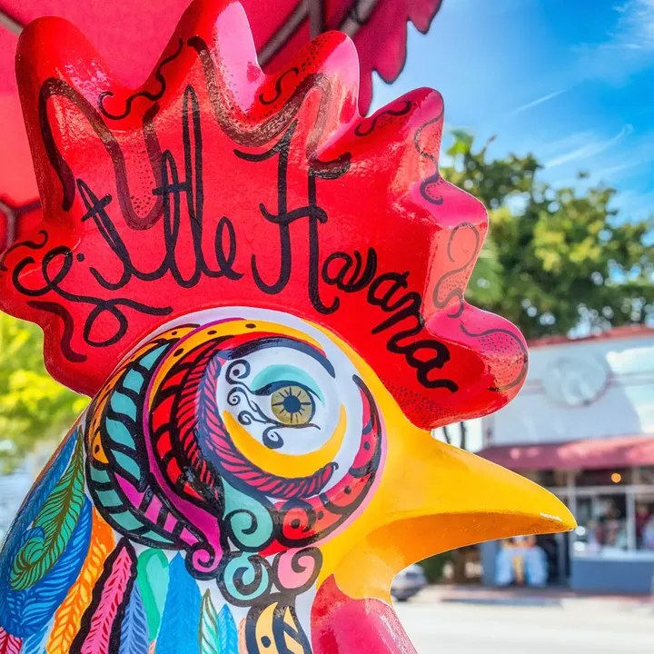 A close-up of the colorful painted face of a rooster sculpture that says Little Havana.