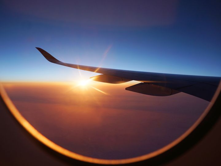 Sunlight peeking out from the clouds is seen through airplane window under the wing during sunrise.
