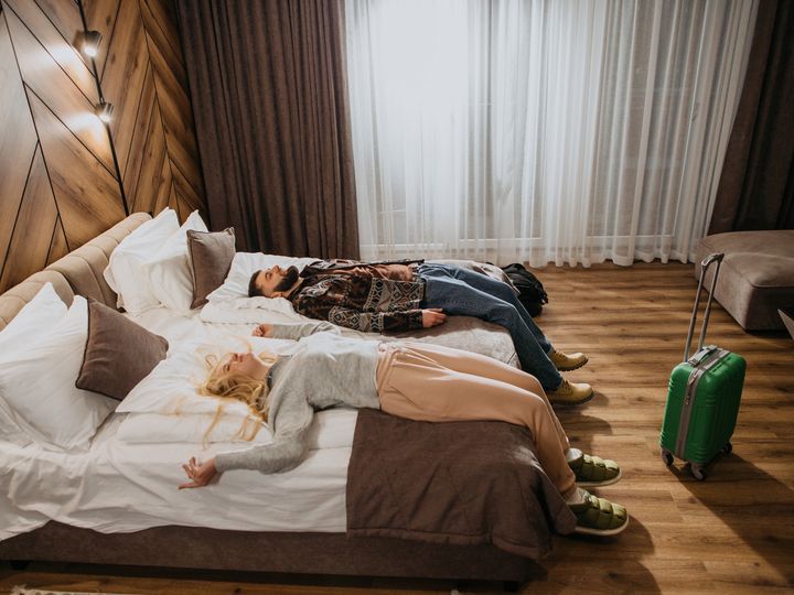 Couple relaxing on a bed with a suitcase near their feet.