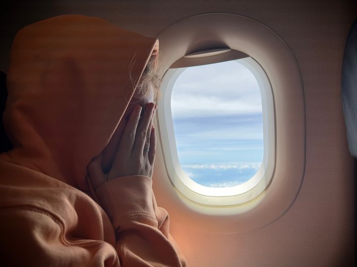 A person on an airplane next to a window covering their face with a hood on.