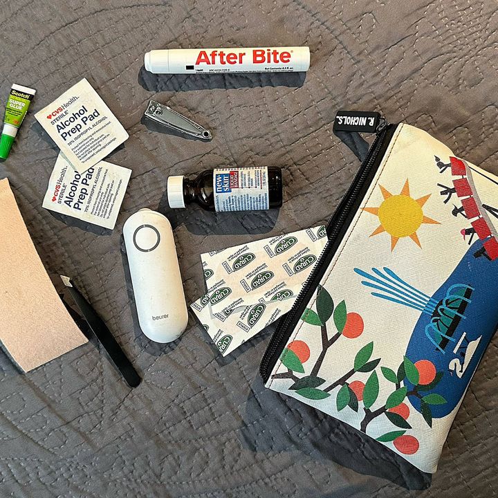 A travel pouch on a blanket surrounded by items such as nail clippers, alcohol pads, bug bite treatments, and super glue.