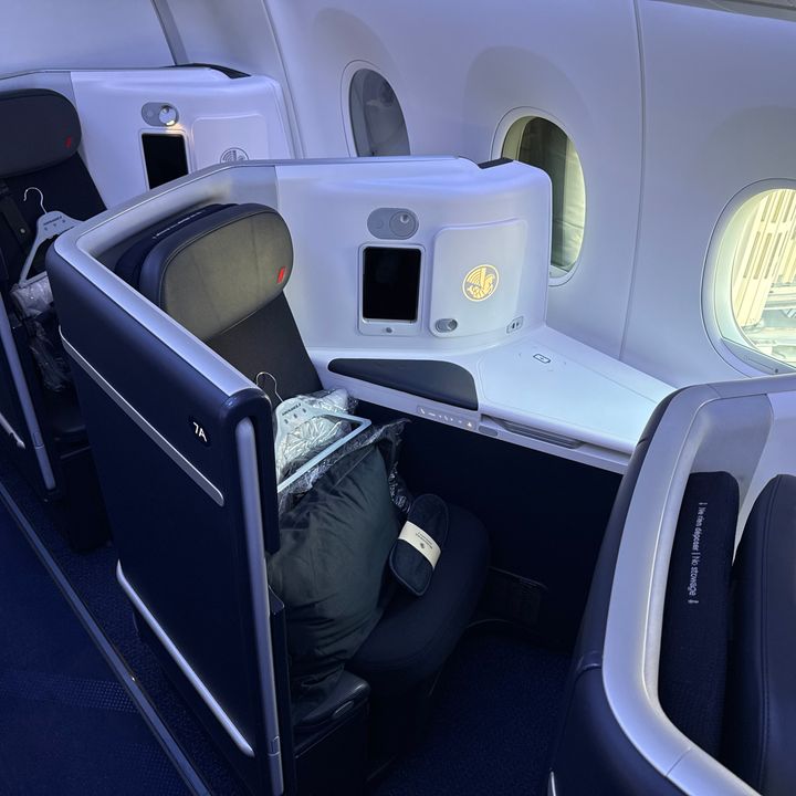 A business class window seat on a cabin on an Air France flight with a hanger and a pillow on the seat.