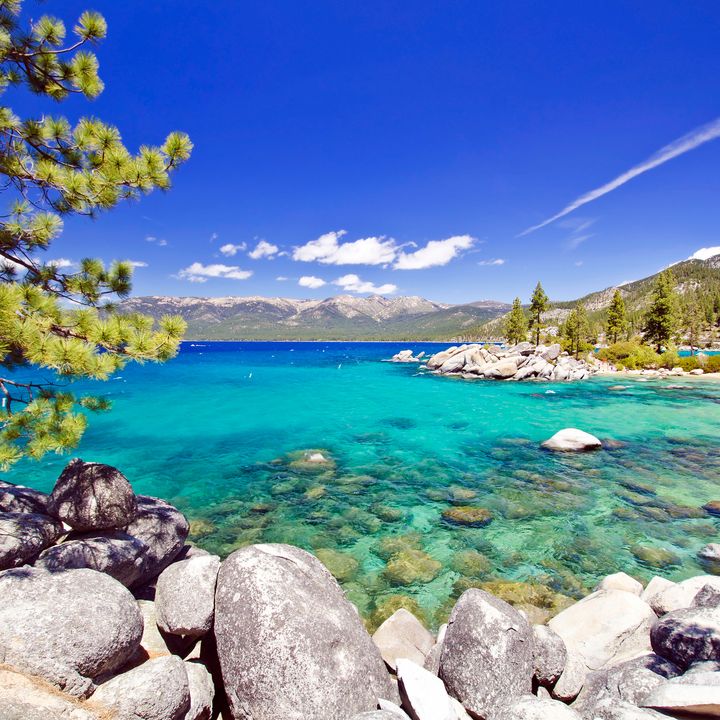 A shoreline along Lake Tahoe with clear bright blue water and a rocky water’s edge.