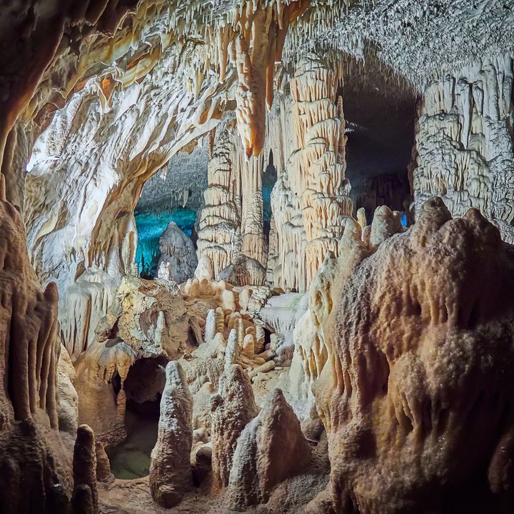 A view of stalactites and stalagmites in an underground cavern that’s partially lit up and dark in other places.