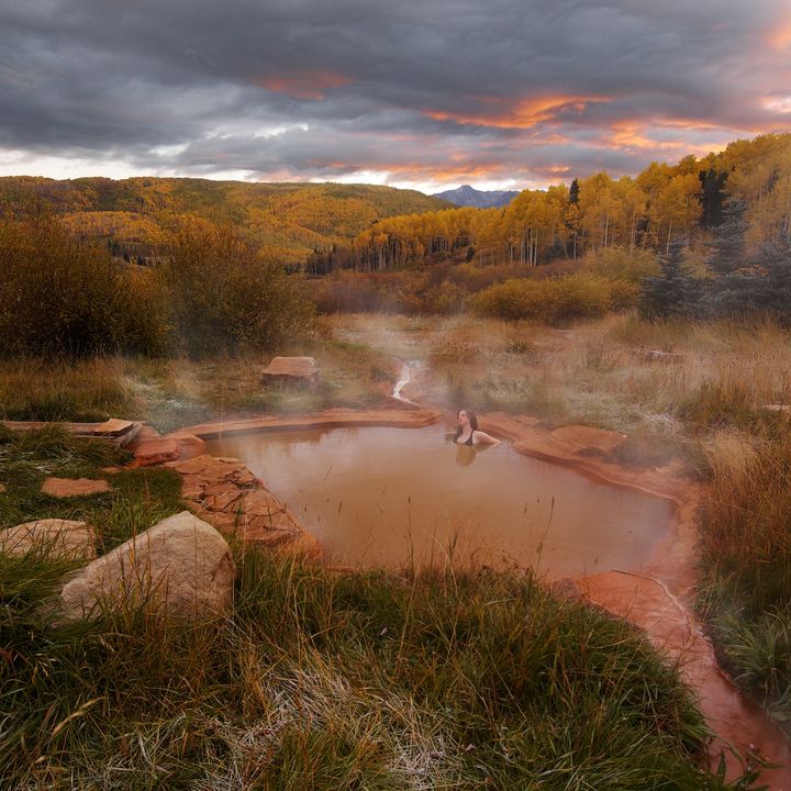 Steaming natural hot springs outside the bathhouse at Dunton Hot Spring, with dusk gray skies and forest in the background.