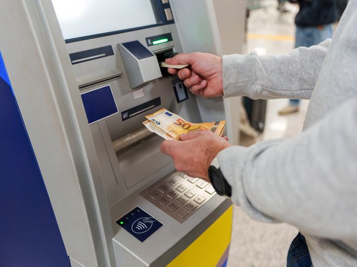 A person at an ATM with only arms visible taking out Euros.