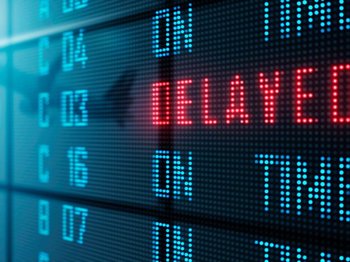 A flight status board in an airport says ‘delayed’ in red.