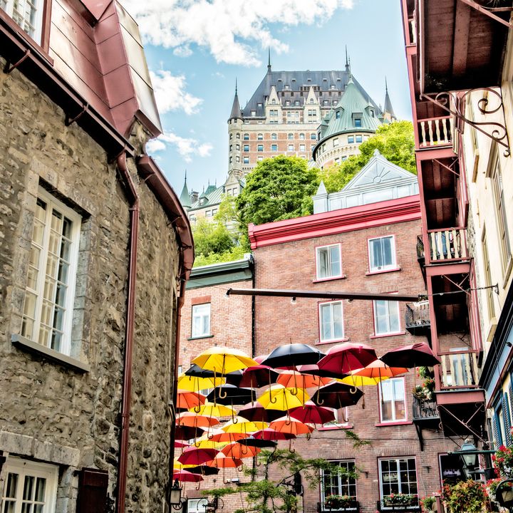 A view of Petit Champlain Street in Quebec City, Canada, with historic stone buildings on each side, decorative umbrellas, and a peek through at The Fairmont Chateau Frontenac.