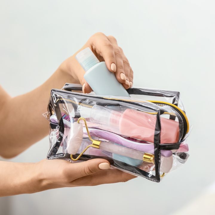 Female hands holding a cosmetics bag full of toiletries against a light background.