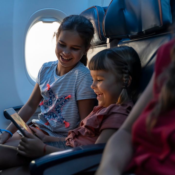 Two little girls travel by plane and look at an ipad next to the window.