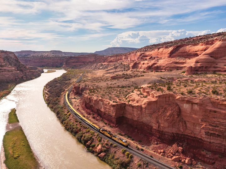 A Canyon Spirit train next to a river and Utah's red rock formations.