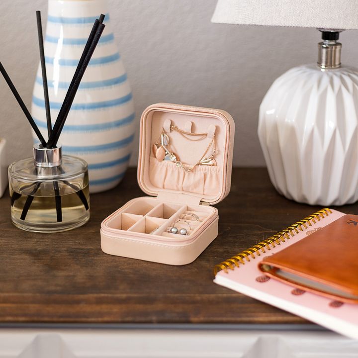 A small compact jewelry case sitting on a dresser next to a lamp, notebook, aromatherapy sticks, and a succulent.